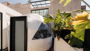 Una estructura moderna, blanca y semicerrada con ventanal de vidrio, junto a un edificio con grandes ventanales y fachada de hormigón.