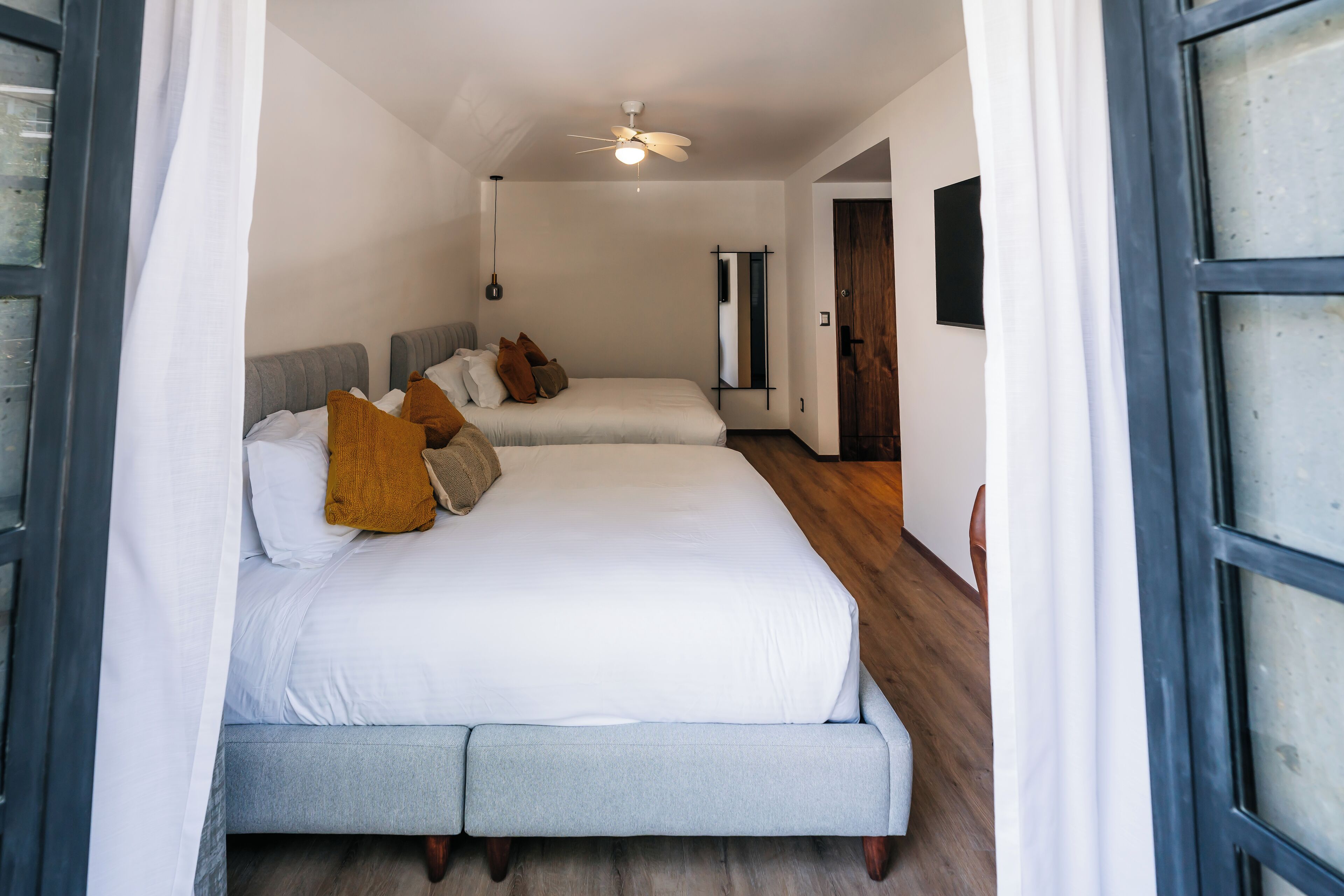 A bedroom with two beds, a ceiling fan, and a wooden floor.