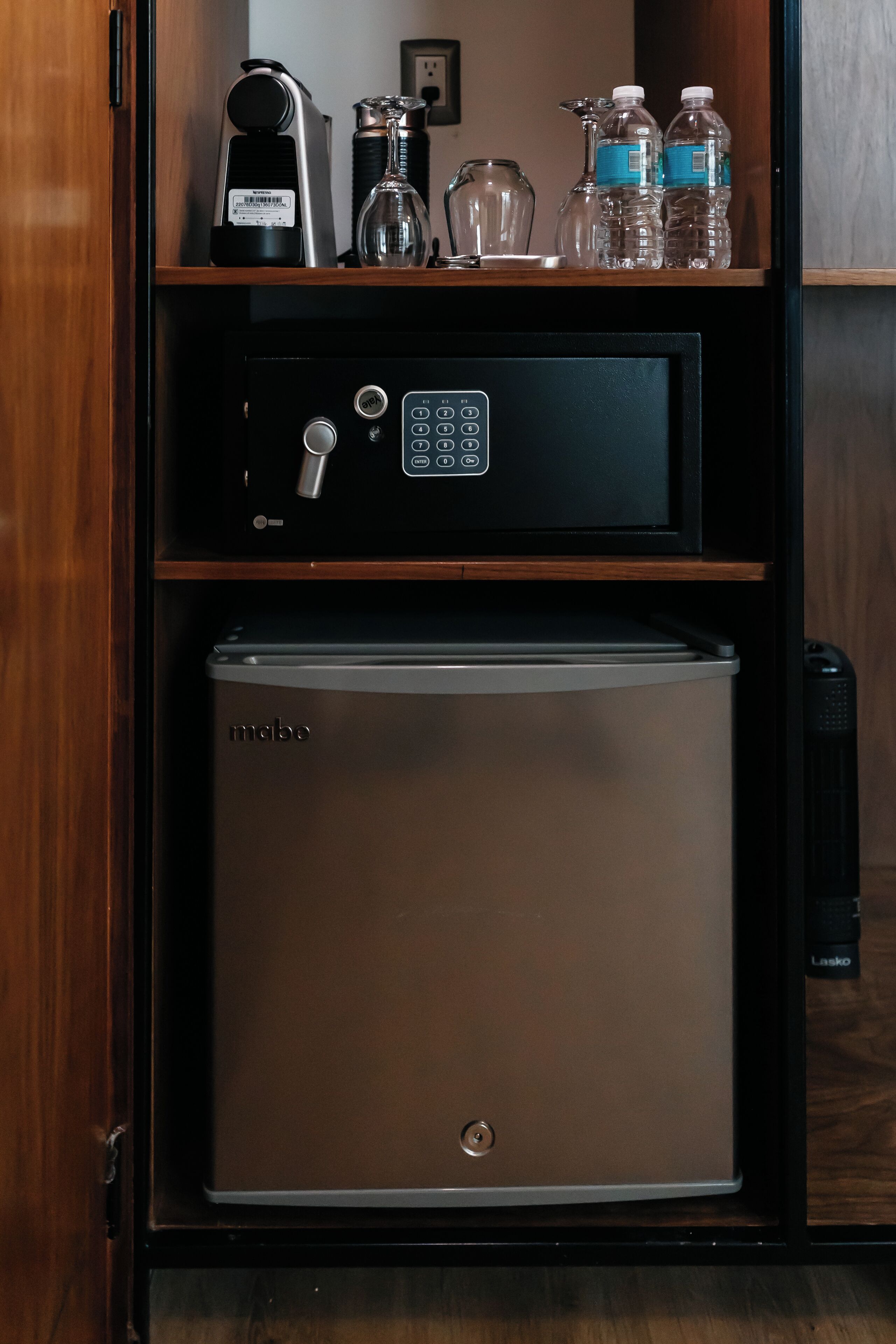 Un minibar con un refrigerador, una cafetera y varias botellas de agua.