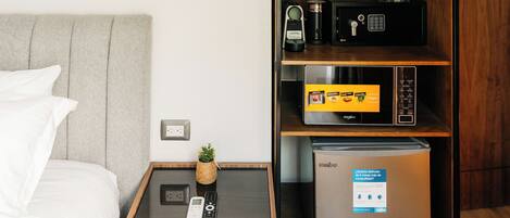 A hotel room with a bed, a bedside table with a remote control, a minibar, and a built-in refrigerator.