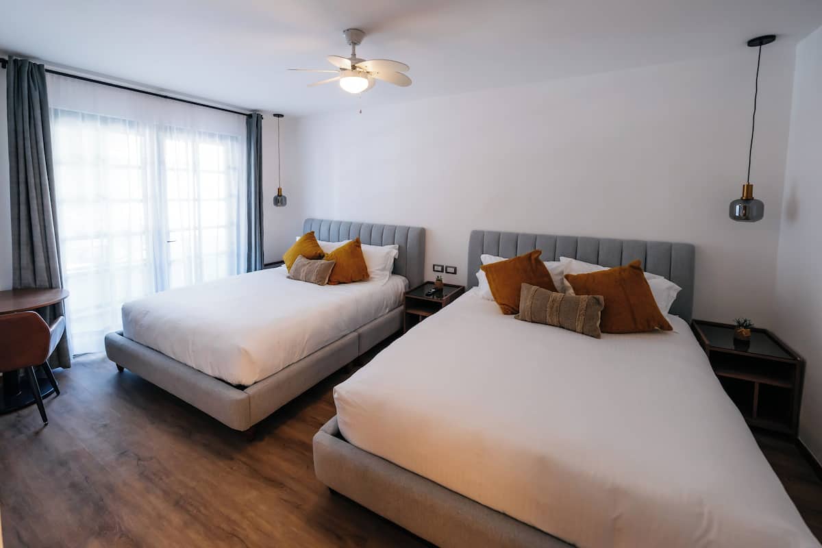 A hotel room with two beds, a desk, and a ceiling fan.