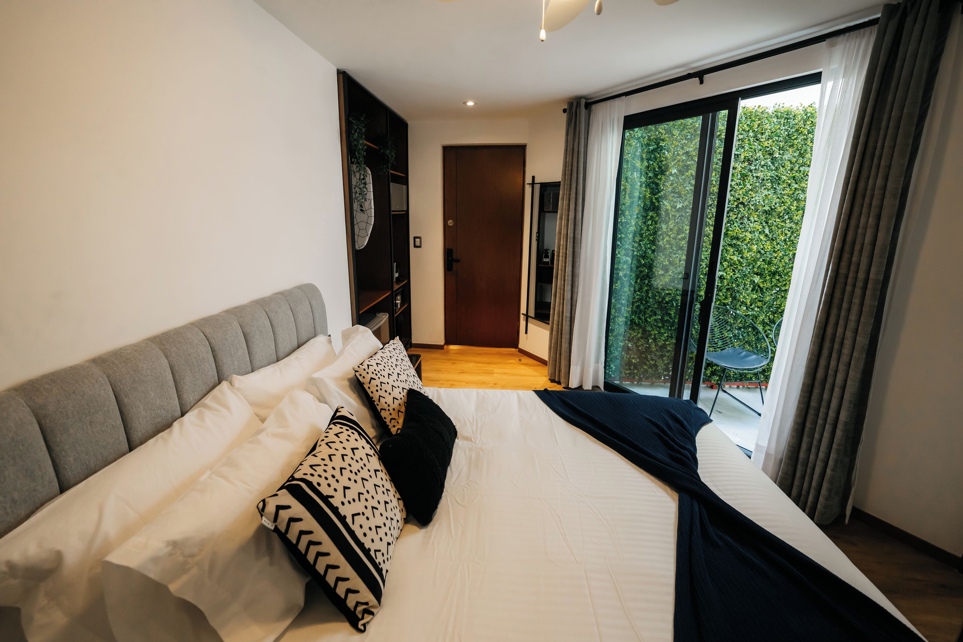 A modern bedroom with a large bed, a wardrobe, and a view of greenery through a sliding door.