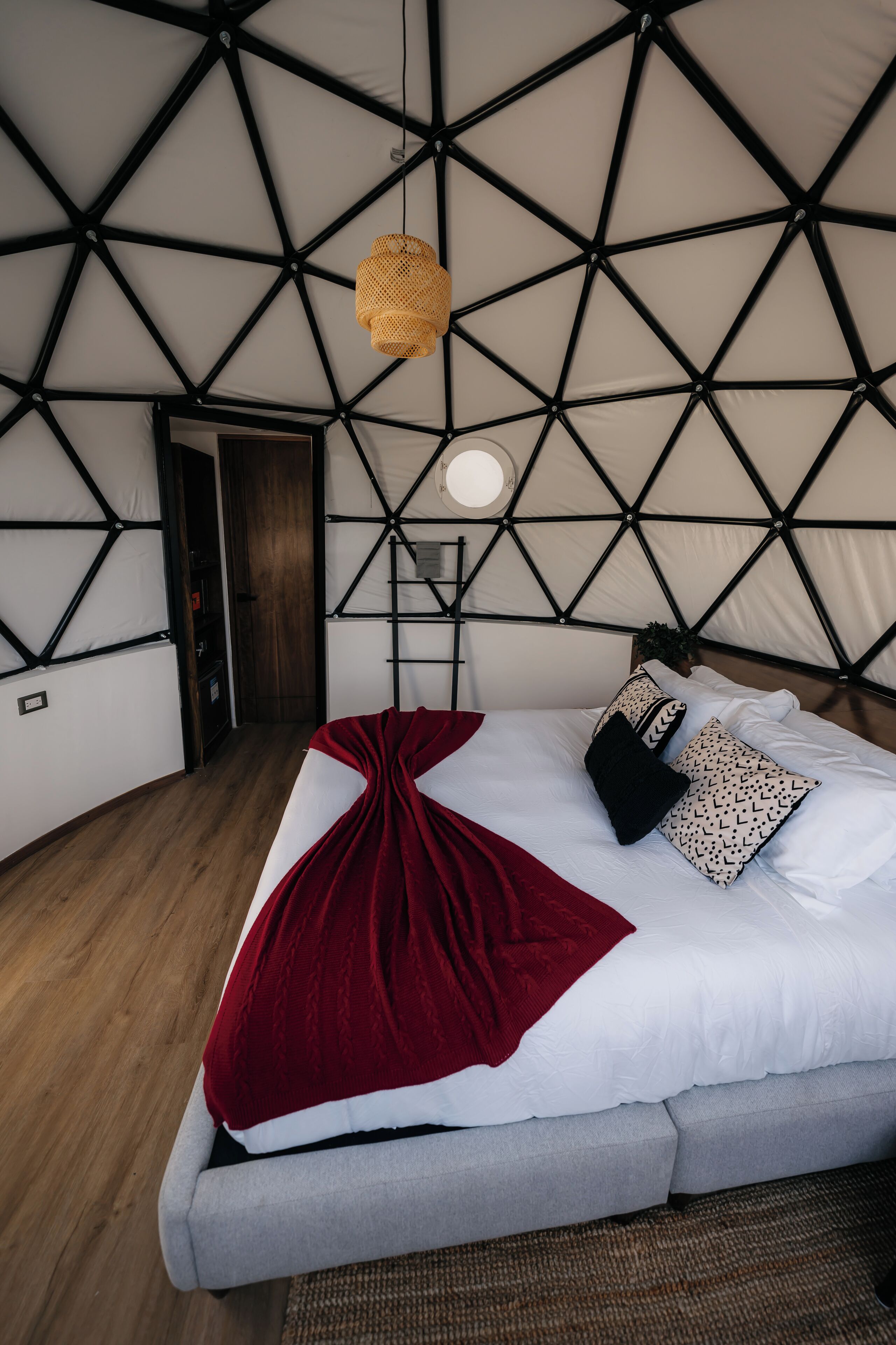 A modern, geometric-patterned tent-style room with a bed, a hanging light fixture, and a small plant.