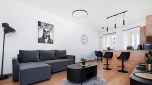 Een moderne woonkamer met een grijze bank, een bijzettafeltje en een eethoek met een houten tafel en stoelen.