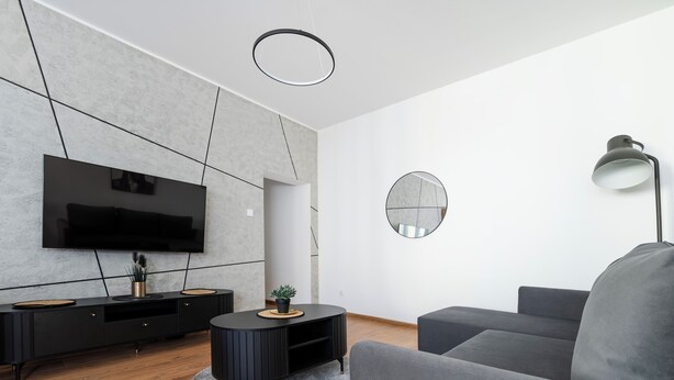 Een moderne woonkamer met een flatscreen televisie, een ronde salontafel en een grijze bank.