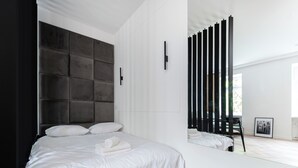 Ein modernes Schlafzimmer mit einem großen Bett, einem dunklen Kopfteil, einem Spiegel und einem Holzboden mit Fischgrätmuster.