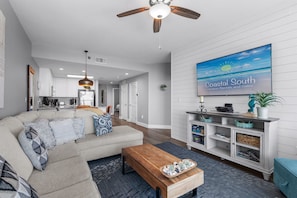 A modern living room with a sofa, coffee table, and a TV displaying 'Coastal South Vacation Rentals and Sales.' - 2 Bedroom Lighthouse w/Bunk,  3 Pools! Direct Beachfront.  Free Daily Activities (Gulf Shores)