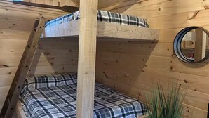 A bunk bed with plaid bedding in a wooden room with a window and a round mirror on the wall.