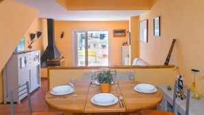 A dining area with a wooden table set for four, surrounded by orange chairs. A potted plant is on the table, and there are wine glasses and plates. - WELCS CASA ADOSADA 241 EMP con terraza al canal (Empuriabrava)