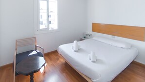 A bedroom with a wooden floor, a bed with white linens, a nightstand, a chair, and a window with blinds. - WELCS CASA ADOSADA 241 EMP con terraza al canal (Empuriabrava)