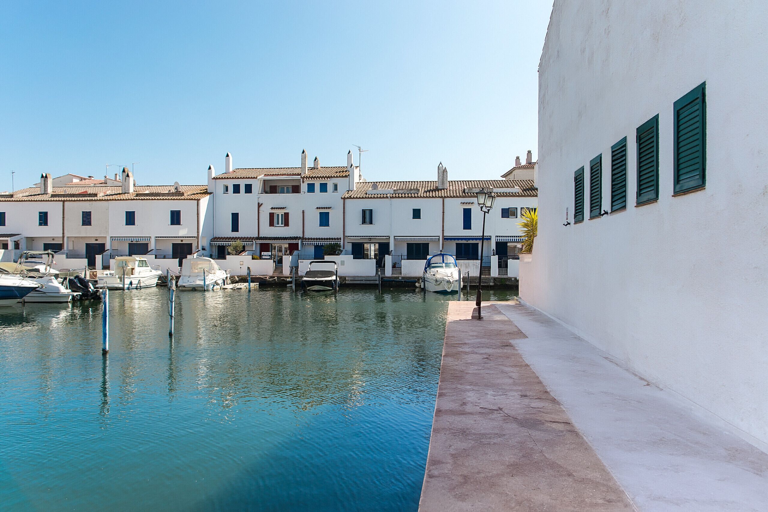 A marina with boats docked, a white building with green shutters, and a clear blue sky.