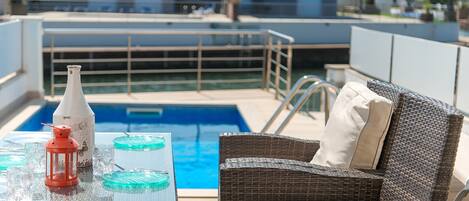 A poolside area with wicker furniture, a glass table, and a bottle.