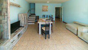 A dining area with a table and chairs, a television on a wooden stand, and a sofa. - WELCS CASA 242 EMP con piscina y vista al canal (Empuriabrava)