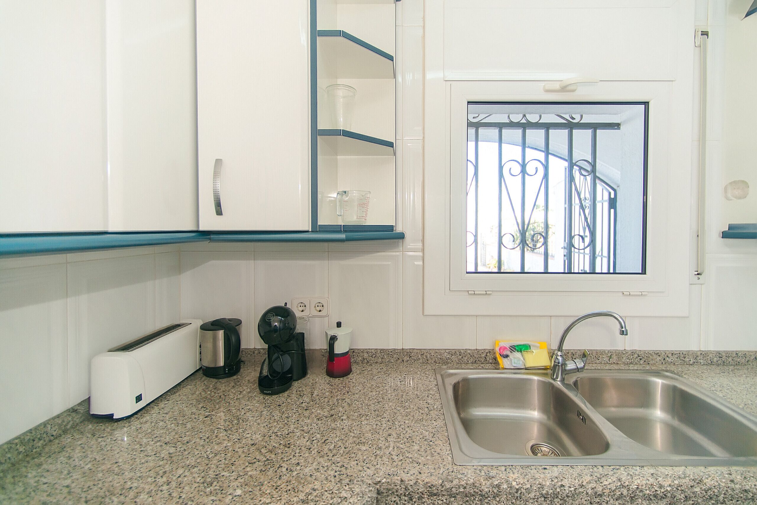 A kitchen with white cabinets, a granite countertop, a toaster, a coffee maker, a kettle, and a sink.