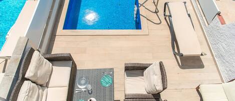 A poolside area with a sun lounger, a table with a glass top, and a pool.