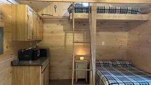 Een klein houten vakantiehuisje met een stapelbed, een kitchenette en een ladder.