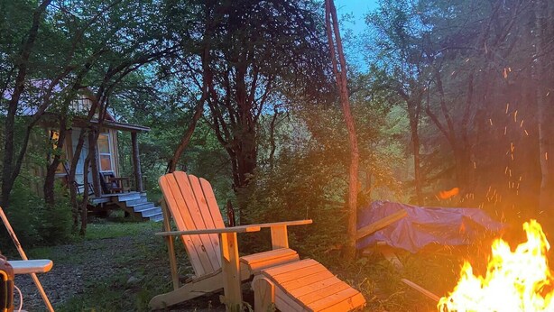 Een camping met houten stoelen, een vuurkuil en een blokhut op de achtergrond.