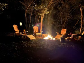 En lägereld med fyra trästolar placerade runt omkring, i en skogsmiljö.