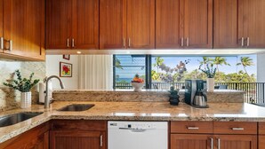 A kitchen with wooden cabinets, granite countertops, a dishwasher, and a coffee maker.