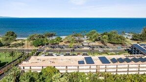 A coastal building with solar panels on the roof, parking lots, and a view of the ocean.