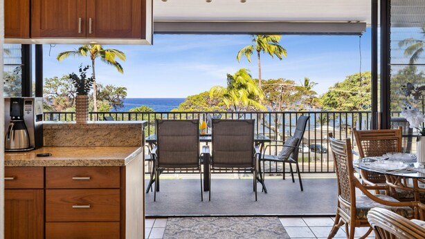 A balcony with a view of the ocean, a dining table with chairs, and a coffee maker.
