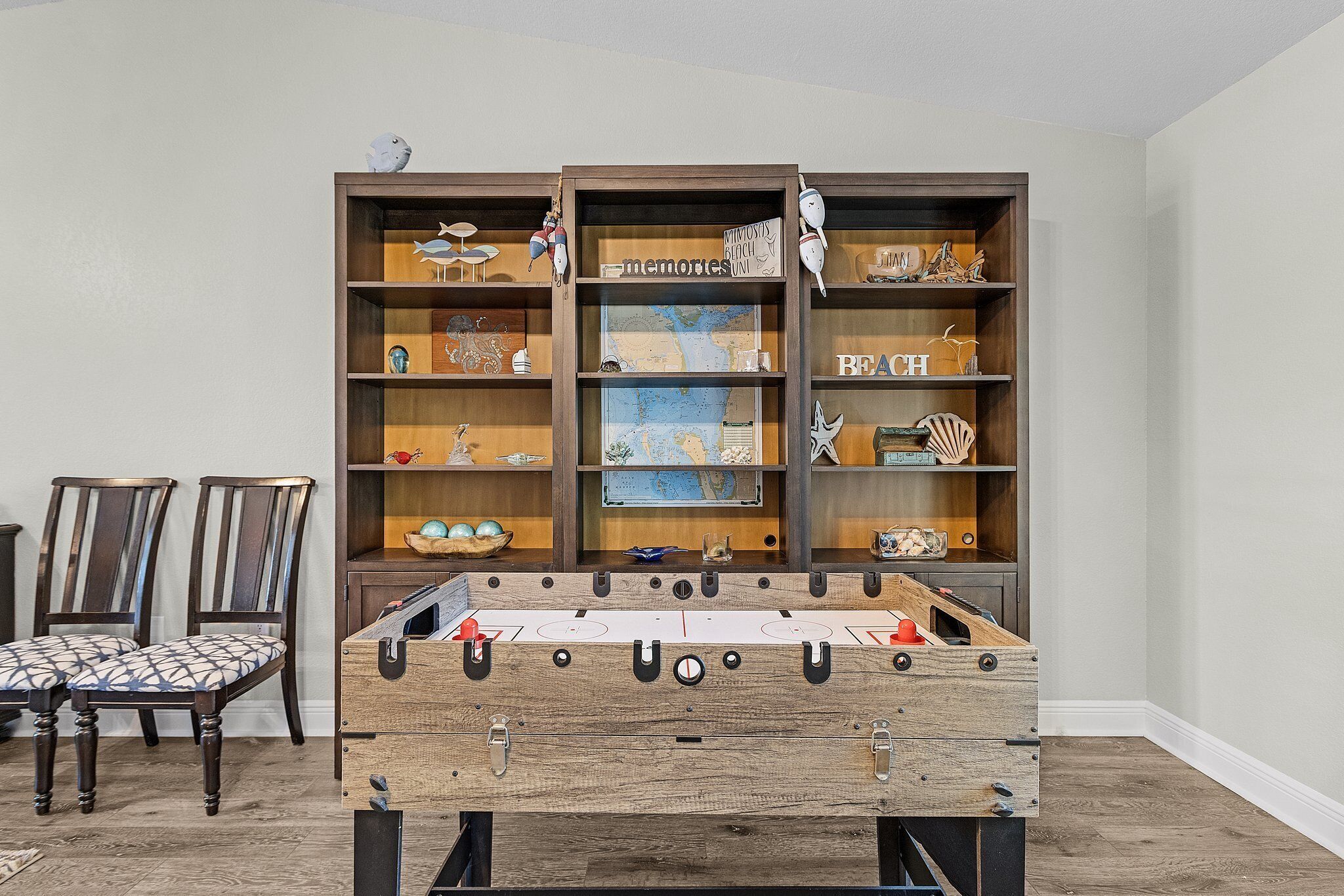 Une pièce avec une table de baby-foot, des chaises en bois et une bibliothèque remplie de divers objets.