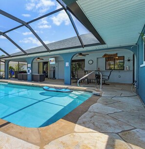 Ein Poolbereich mit klarem, blauem Pool, Steinböden und einer überdachten Sitzgelegenheit mit Stühlen und Tisch.