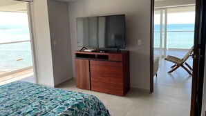 Un dormitorio con cama, cómoda de madera, televisor y vista al mar a través de una puerta corrediza.
