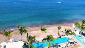 Un complejo turístico en la playa con piscina, palmeras y vista al océano.