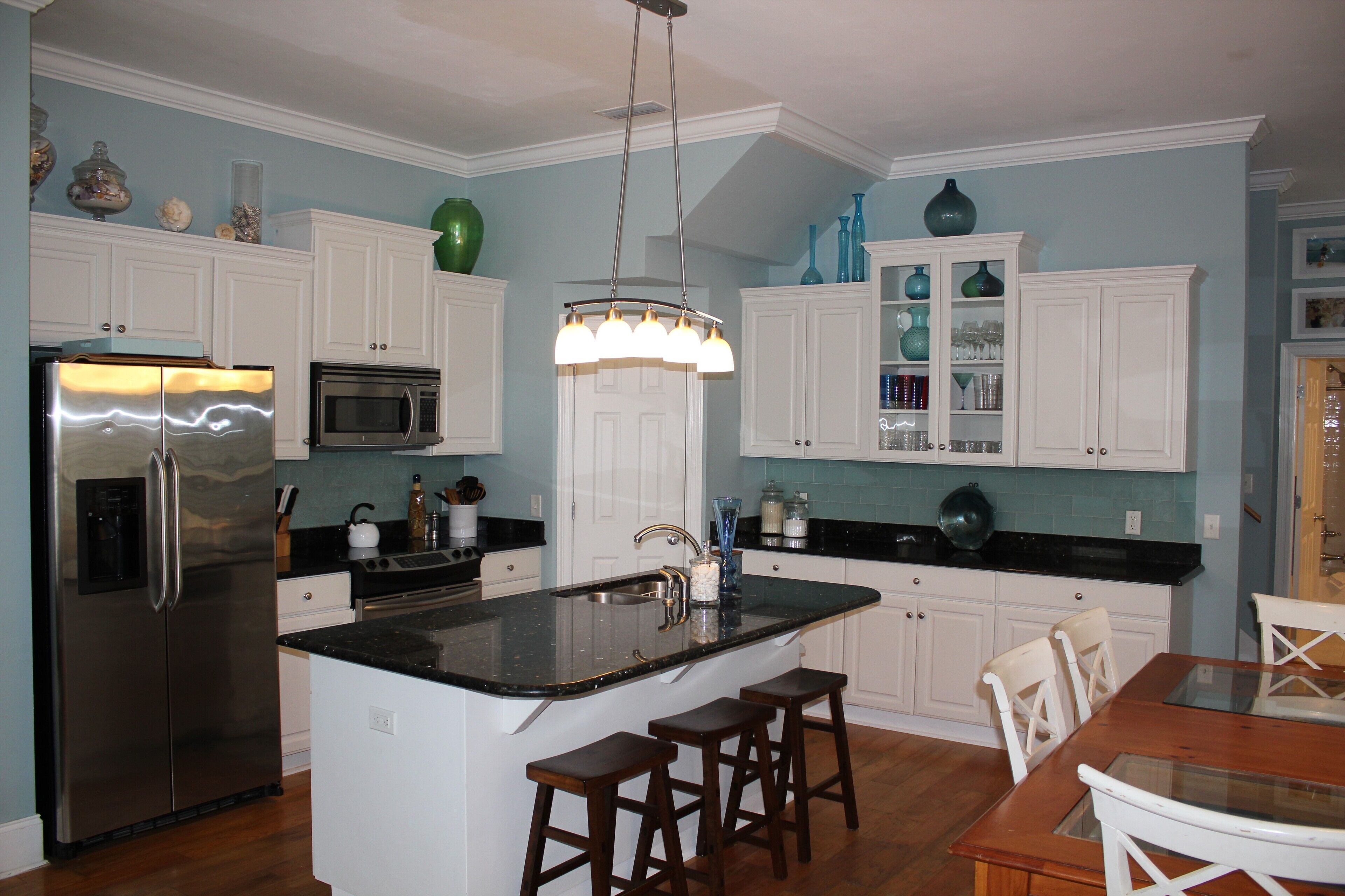 A modern kitchen with white cabinetry, a stainless steel refrigerator, a microwave, and a central island with stools.