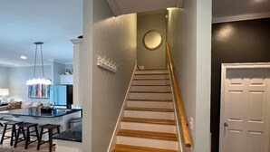 Un escalier avec des marches en bois et une rampe, menant à une pièce dotée d’une porte blanche et d’un interrupteur sur le mur.