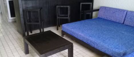 Et værelse med en sofa, et lille bord og to stole. Der er et tekøkken med vask og komfur.