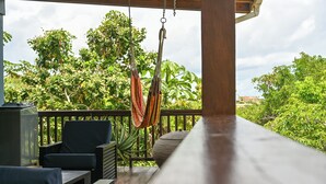 Une terrasse en bois avec des meubles d’extérieur, un hamac et une végétation luxuriante en arrière-plan.