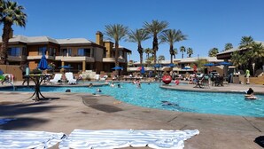 A pool area with lounge chairs and umbrellas, surrounded by palm trees and a building with multiple balconies. - MARRIOTT DESERT SPRINGS VILLAS 1 LOCKOUT, PALM DESERT, #1 RATED MARRIOTT RESORT (Palm Desert,)