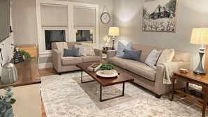 Un salon avec deux canapés, une table basse, une lampe, une horloge et un tableau accroché au mur.