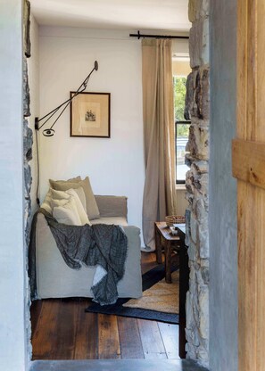 Une pièce confortable avec un lit, un tableau encadré au mur, une fenêtre avec des rideaux et un mur en pierre.