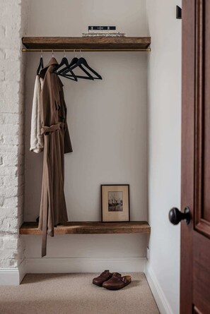 A room with a wooden shelf holding books and a framed picture, a coat rack with a coat, and a pair of shoes on the floor. - The Top Floor at Collected Places Hobart (North Hobart)