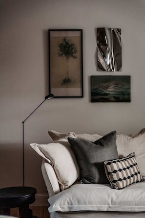 Una sala de estar moderna con un sofá, cojines, una lámpara de pie y cuadros en la pared.