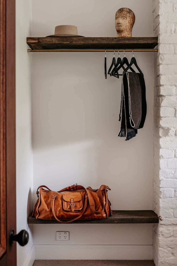 A wall-mounted shelf with a wooden hat and a brown leather bag.