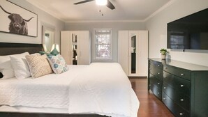 Un dormitorio con cama, cómoda, ventilador de techo y ventana.