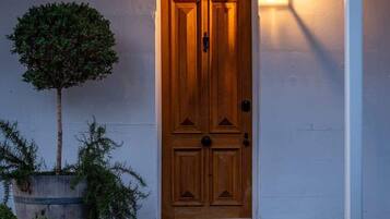 Una puerta de madera con el número 75 arriba, un pequeño porche con escalones y un árbol en maceta a la izquierda.
