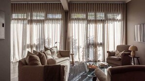 Ein modernes Wohnzimmer mit einer Couch, Sesseln, einem Couchtisch und großen Fenstern mit durchsichtigen Vorhängen.