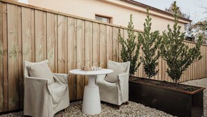 A patio with two white chairs, a small round table, and a planter with small trees.