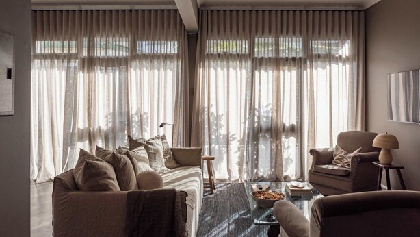 A modern living room with a sofa, armchairs, a coffee table, and sheer curtains.