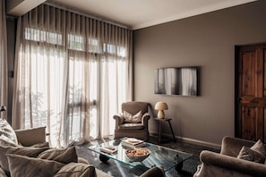 A living room with a glass coffee table, a sofa, a chair, a lamp, and a painting on the wall.