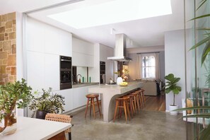 Una cocina moderna con una isla central, taburetes de bar y un ventanal grande.