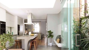 A modern kitchen with a central island, bar stools, and a large potted plant.