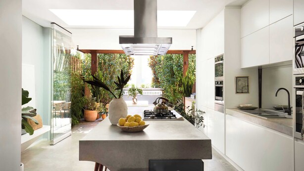 A modern kitchen with a central island, a built-in stove, and a view of a lush garden through a glass door.
