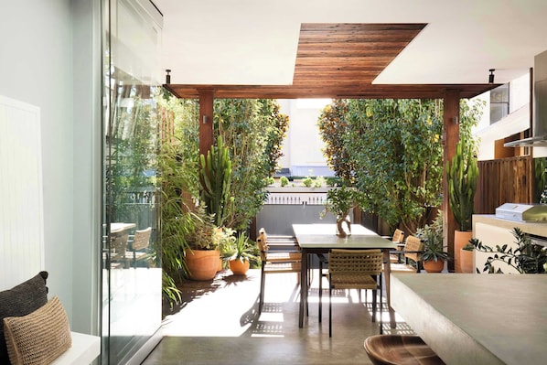 Un patio al aire libre con techo de madera, una mesa, sillas y plantas en macetas.