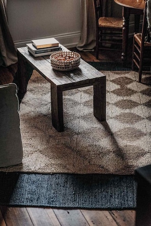 A wooden coffee table with a woven rug, a basket of cookies, and a book on it.